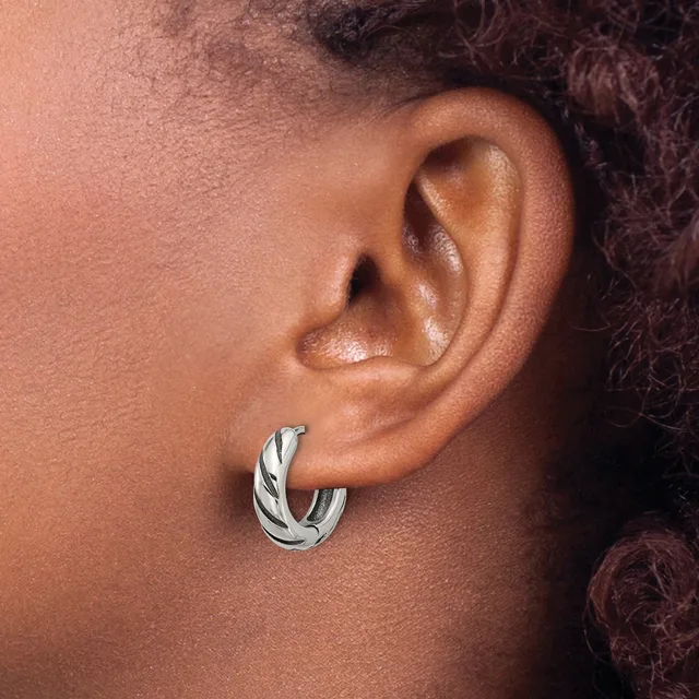 A twisted silver hoop earring worn in the earlobe of a person with medium-deep skin tone and dark curled hair.
