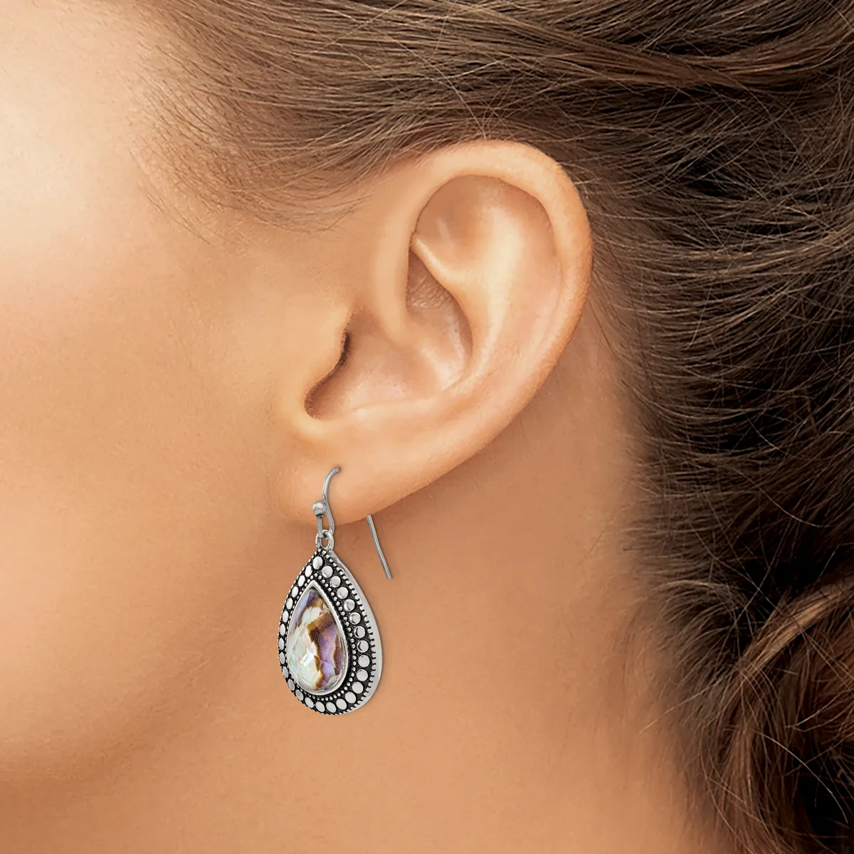 A teardrop-shaped silver earring with a pale iridescent stone center surrounded by small rhinestones, worn on a model's ear.