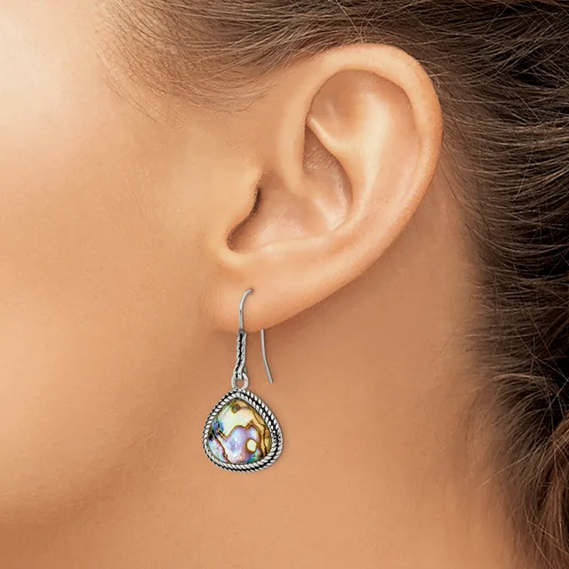 A woman wearing a teardrop-shaped dangle earring with an iridescent stone center surrounded by a beaded silver-tone metal frame.
