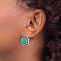 A person wearing a silver square earring with a turquoise stone and decorative beaded border, shown on their ear from the side.