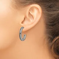 A woman wearing a silver hoop earring with a textured, paved surface sits in profile showing her ear and dark hair.