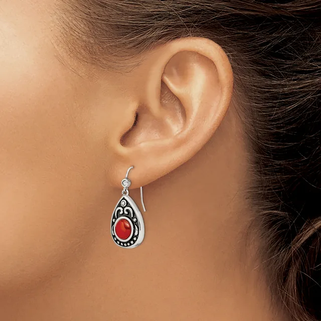 A silver teardrop earring with ornate scrollwork and a red stone center hangs from a woman's earlobe.