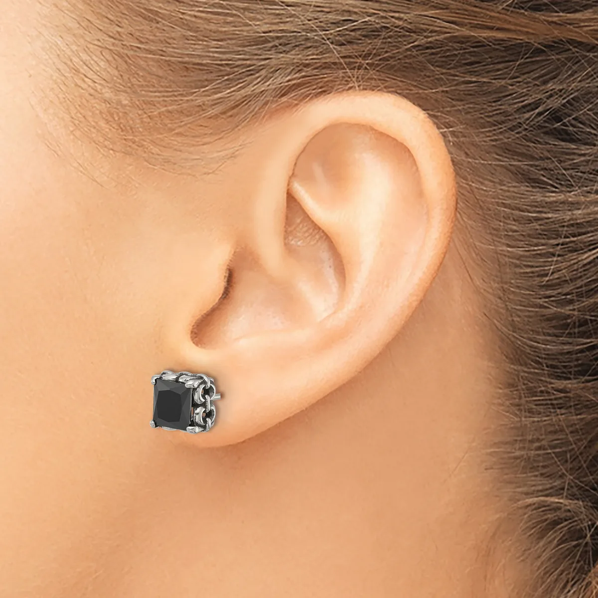 A close-up view of a black square gemstone earring with decorative silver-toned metalwork, worn on a person's earlobe.