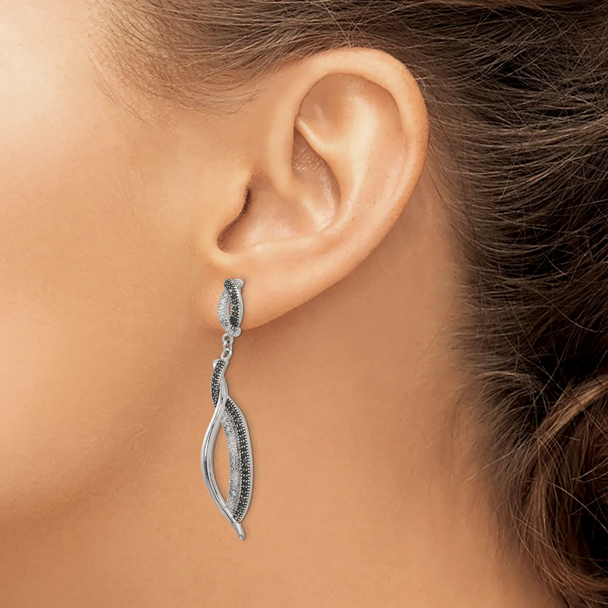A silver drop earring with a twisted leaf design and small gemstones is worn on a model's earlobe.