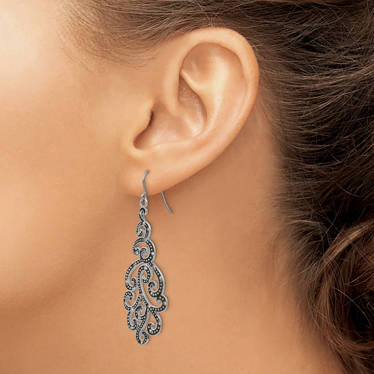 A woman wearing an ornate silver chandelier-style earring with scrollwork filigree and small diamonds, shown from the side profile of her face and ear.