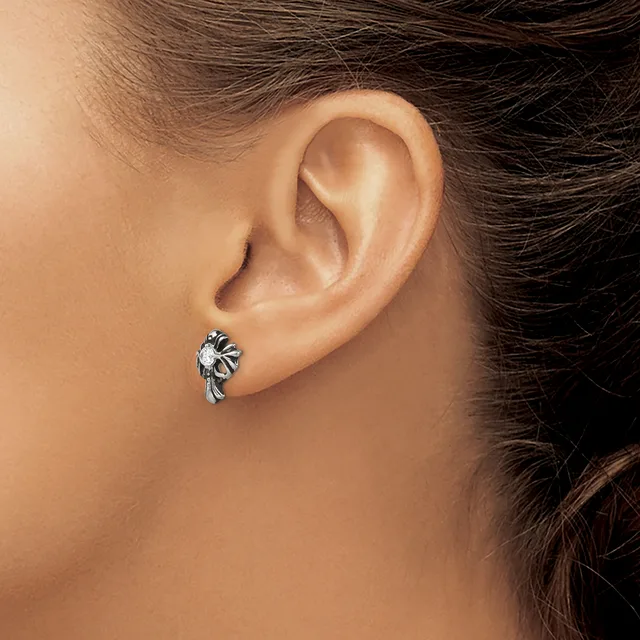 A silver stud earring with an ornate leaf or floral design worn on a person's earlobe, shown in close-up against their neck and shoulder.