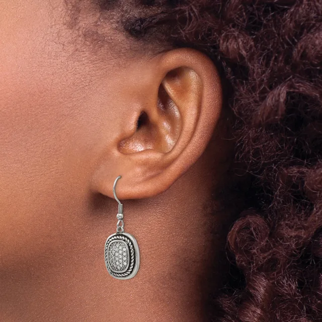 A person wearing a silver oval dangle earring with a textured surface and black enamel outline on a fish hook wire.