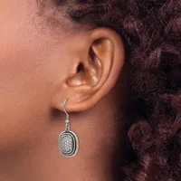A person wearing a silver oval dangle earring with a textured surface and black enamel outline on a fish hook wire.