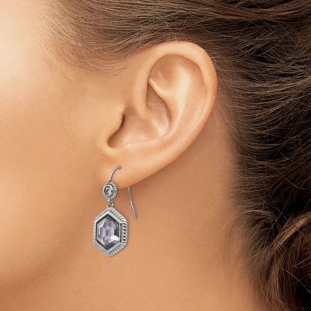 A person wearing a silver drop earring with a hexagonal clear stone pendant surrounded by decorative beading, shown from the side view of their ear.