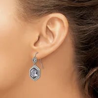 A person wearing a silver drop earring with a hexagonal clear stone pendant surrounded by decorative beading, shown from the side view of their ear.