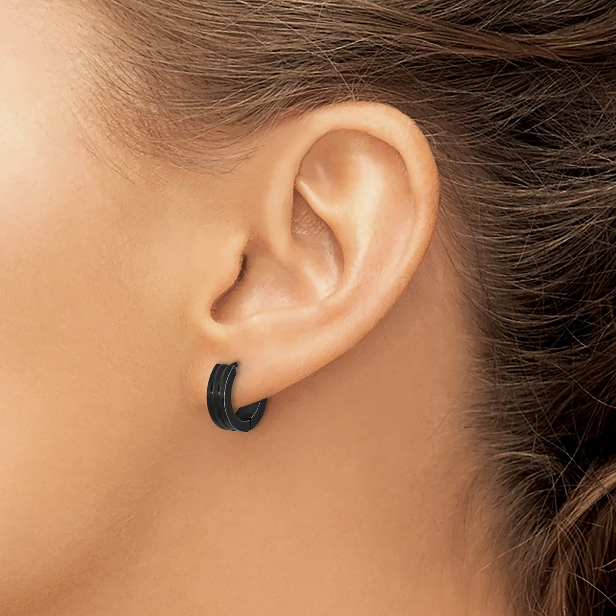 A person wearing a pair of small black curved hoop earrings in their pierced earlobes, shown in profile view.