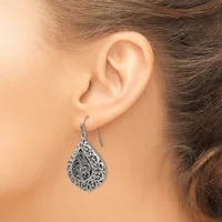 A woman wears a silver teardrop-shaped earring with ornate filigree detailing, suspended from a curved ear wire.