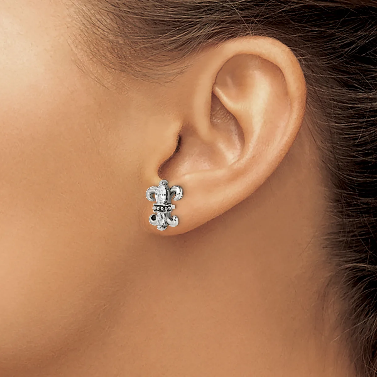 A silver cross-shaped stud earring with circular details at each end, worn on a person's earlobe.