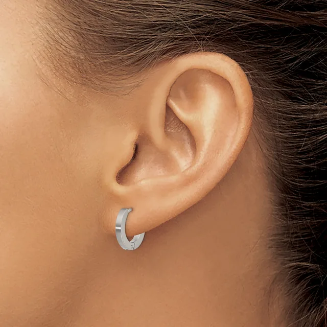 A silver hoop earring with a brushed finish worn on the earlobe of a person with brown hair.