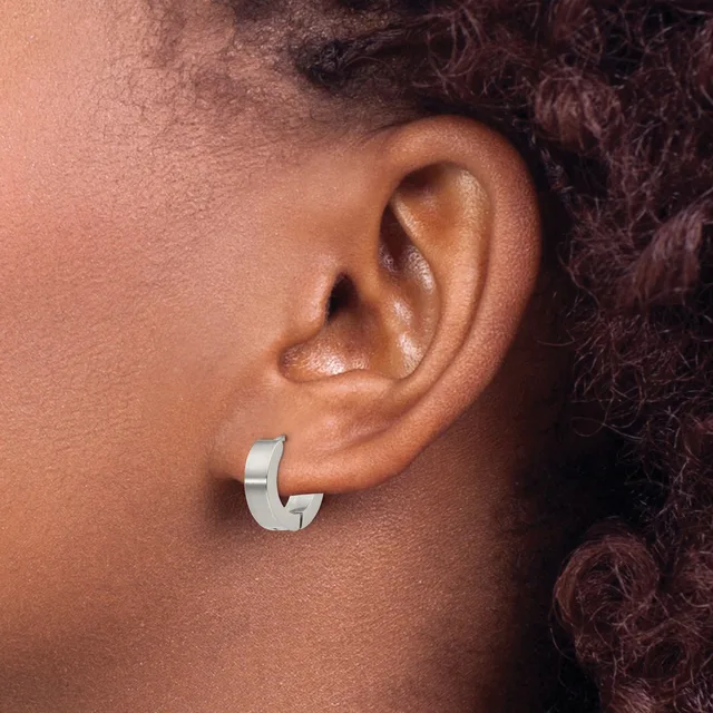 A silver chunky C-shaped hoop earring worn on the earlobe of a person with dark curly hair.