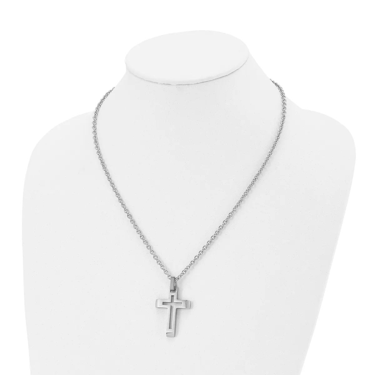 A silver-toned cross pendant hangs from a delicate chain necklace displayed on a white mannequin bust.