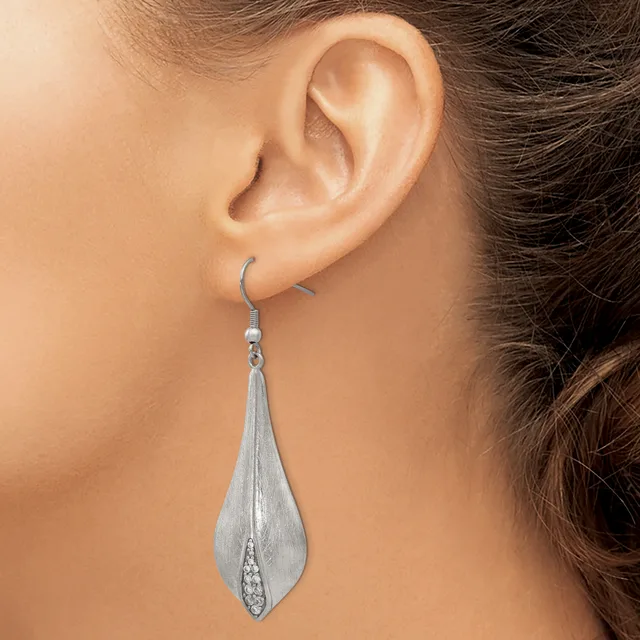 A woman wearing a long teardrop-shaped silver dangle earring with a textured surface and small cubic zirconia stone detail at the base.
