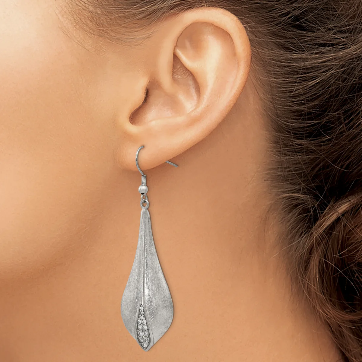 A woman wearing a long teardrop-shaped silver dangle earring with a textured surface and small cubic zirconia stone detail at the base.