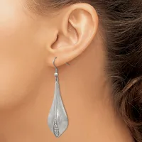 A woman wearing a long teardrop-shaped silver dangle earring with a textured surface and small cubic zirconia stone detail at the base.