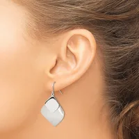 A woman wearing a silver curved square drop earring on a fish hook wire, shown from the side profile of her ear and neck.