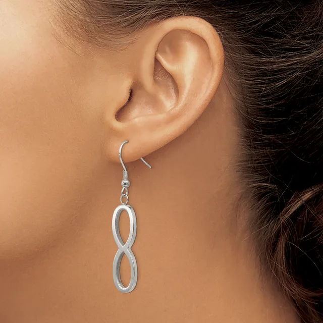 A woman wearing a pair of silver-toned figure-eight drop earrings with French wire hooks.