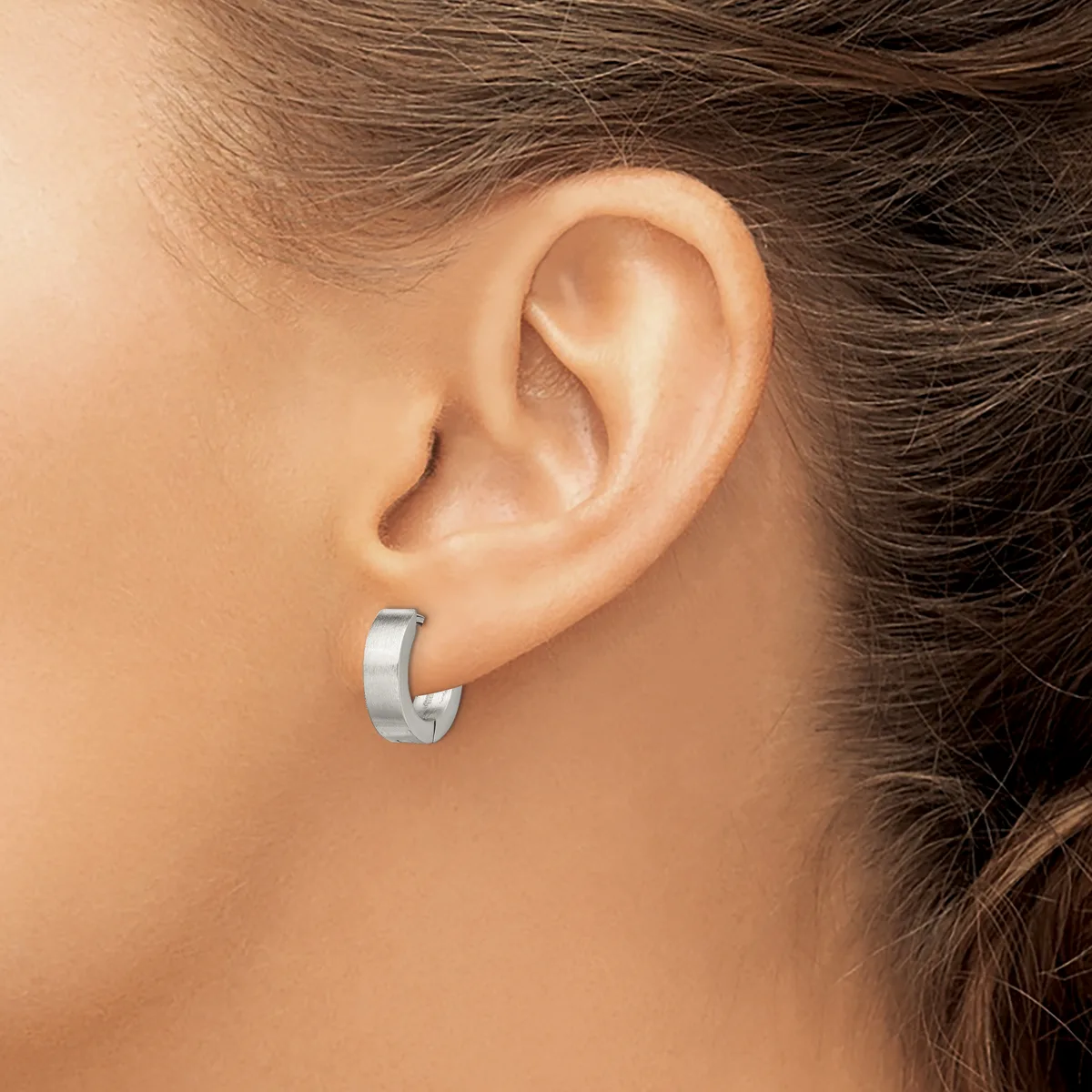 A close-up side view of a person's ear wearing a small polished silver curved hoop earring.