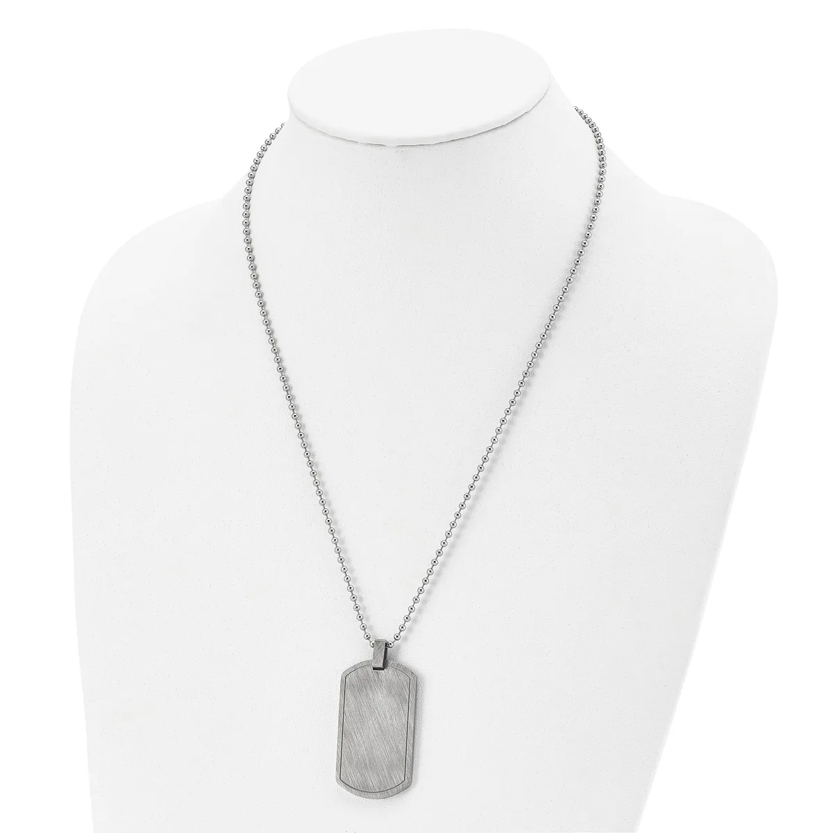 A silver-toned rectangular dog tag pendant hangs from a thin box chain necklace displayed on a white mannequin bust.