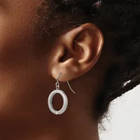 A person wearing a pair of silver oval drop earrings with hook closures, shown from the side view of their ear.