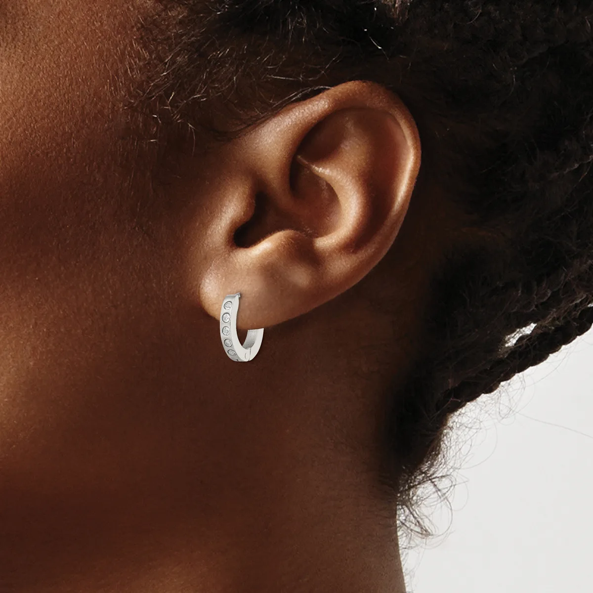 A person wearing a small curved silver hoop earring with a textured surface, shown from the side profile of their ear and neck.