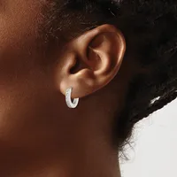 A person wearing a small curved silver hoop earring with a textured surface, shown from the side profile of their ear and neck.