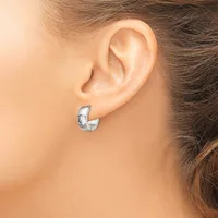 A person wearing small silver hoop earrings with a textured surface, shown from the side view of their ear and neck.