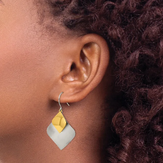 A person wearing a two-tone geometric earring with a yellow curved petal shape on top of a white squared pendant, suspended from a silver hook.