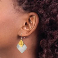 A person wearing a two-tone geometric earring with a yellow curved petal shape on top of a white squared pendant, suspended from a silver hook.
