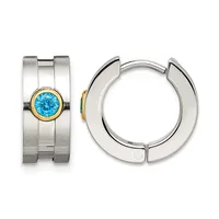 Pair of silver huggie earrings with a brushed finish, one featuring a round blue topaz stone set in a gold bezel on a wide band.
