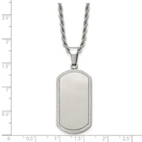 A stainless steel dog tag pendant with a brushed center and textured border hangs from a twisted rope chain against a measurement scale.
