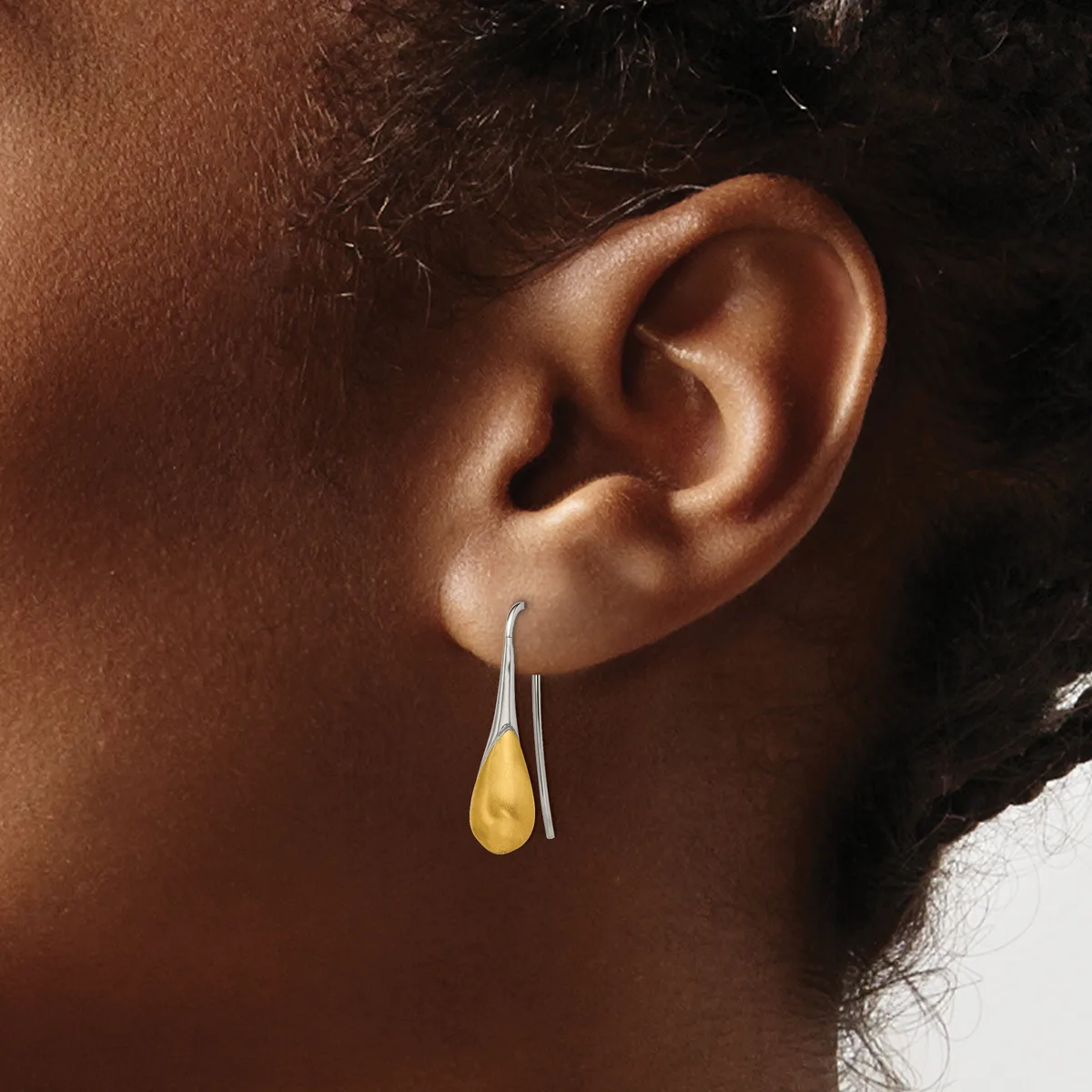 A person wearing a pair of silver hook earrings with amber-colored teardrop pendants hanging from their ears.