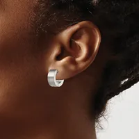 A silver chunky hoop earring worn in the earlobe of a person with brown skin and dark hair, shown in profile against a neutral background.
