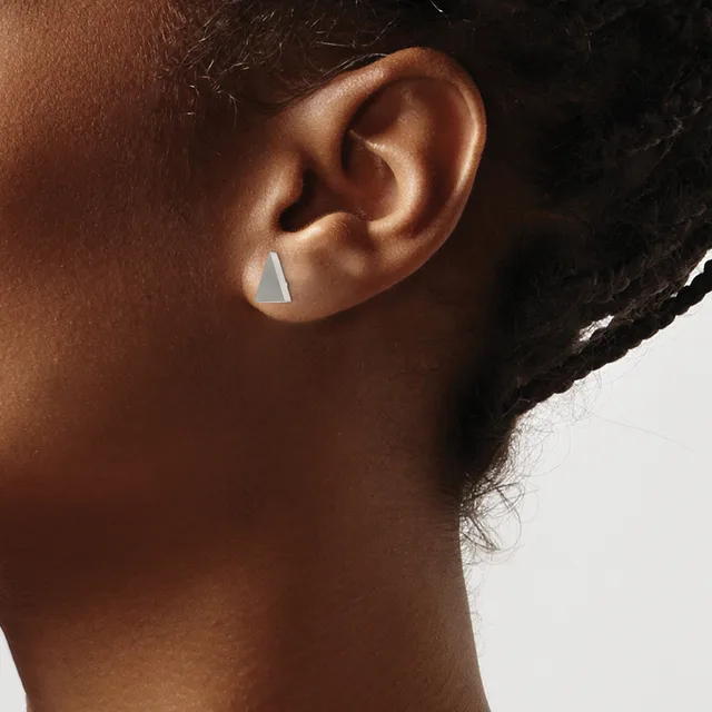 A person wearing a small silver trapezoid-shaped earring in their earlobe, shown in profile against a light background.