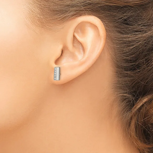 A person wearing a small rectangular silver earring with channel-set stones displayed on their earlobe.