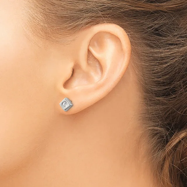 A person wearing a small square silver stud earring with a center stone, shown on their earlobe in profile view.