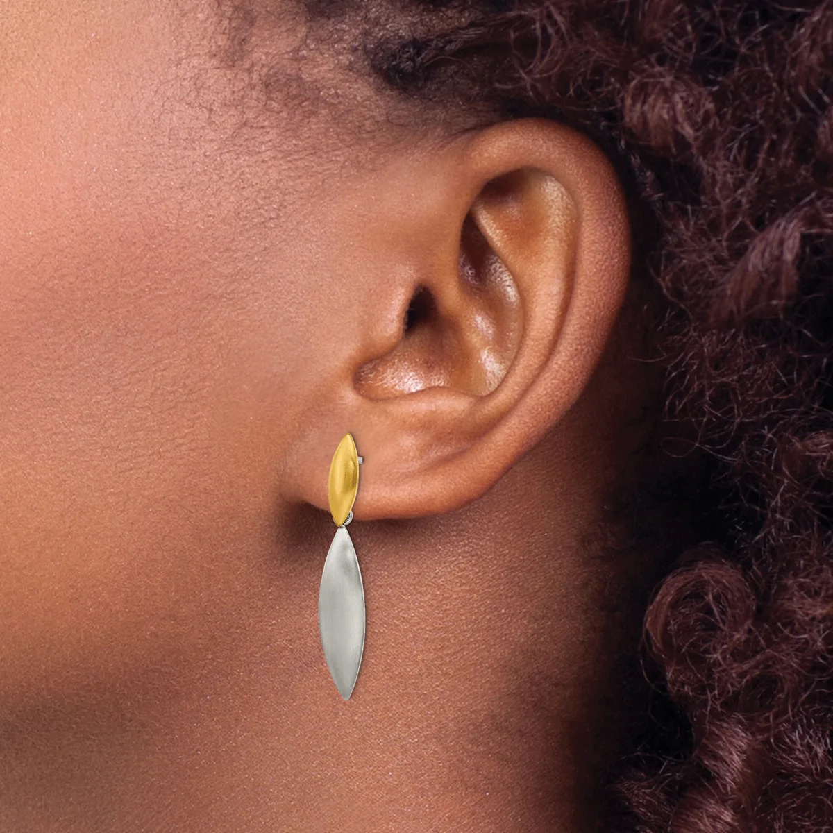 A person wearing a two-tone drop earring with a yellow curved top section and silver elongated bottom section, shown from the side profile near the ear.