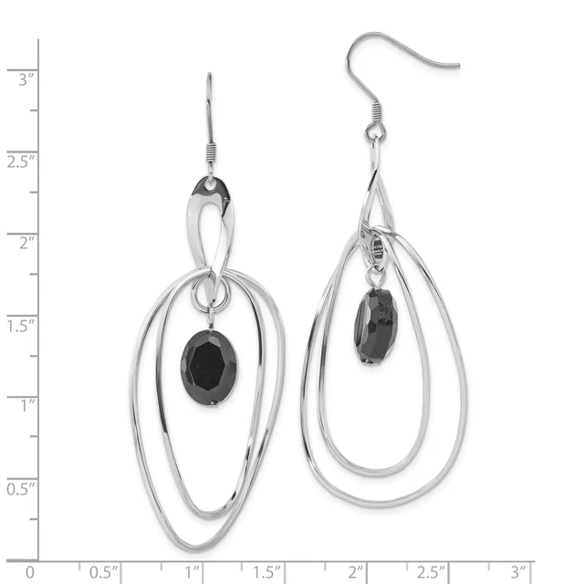 A pair of silver-toned dangle earrings with nested oval loops and small black oval gemstones suspended from fish hook wires, displayed against a measurement scale.