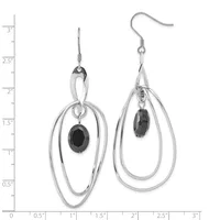 A pair of silver-toned dangle earrings with nested oval loops and small black oval gemstones suspended from fish hook wires, displayed against a measurement scale.