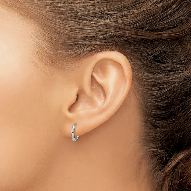 A person wearing small silver hoop earrings, shown from the side with brown hair pulled back to display the ear and earring.