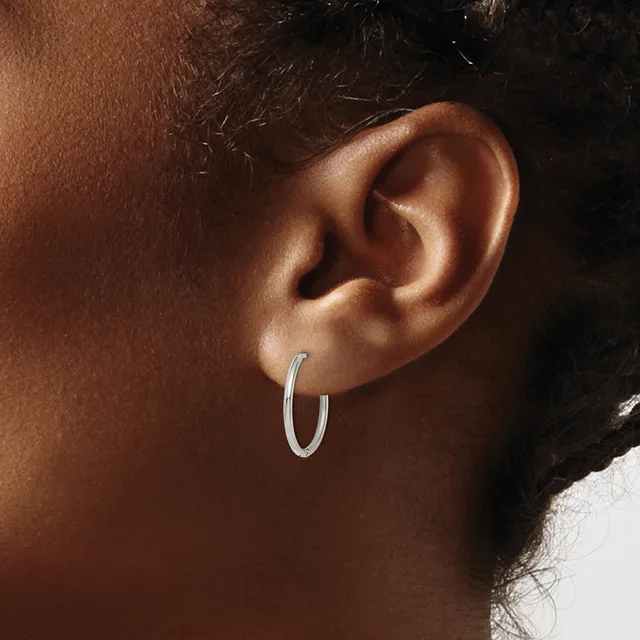 A person wearing a pair of silver hoop earrings, shown from the side profile of their head and ear.