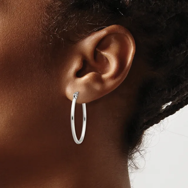 A person wearing a pair of polished silver hoop earrings, shown from the side profile of their ear and neck.