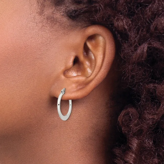 A person wearing a small silver hoop earring in their earlobe, shown in profile view against their ear and dark curled hair.