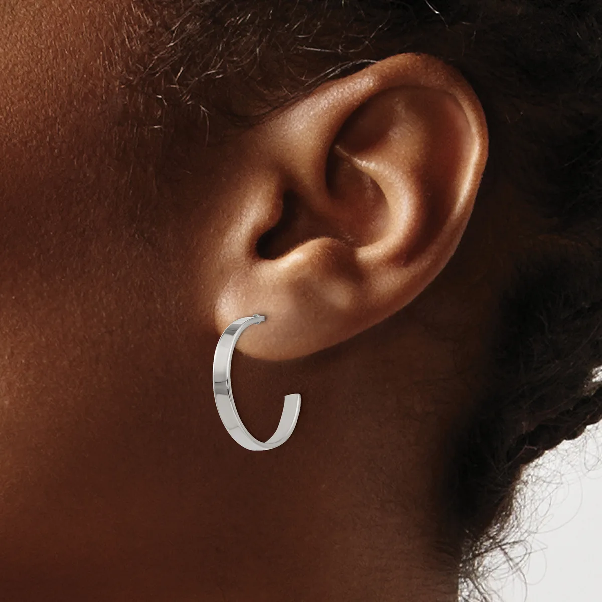 A silver hoop earring worn on the earlobe of a person with medium-toned skin.