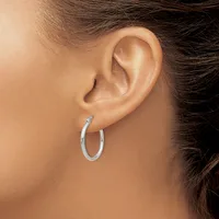 A woman wearing a silver hoop earring in her earlobe, shown from the side profile of her head and neck.