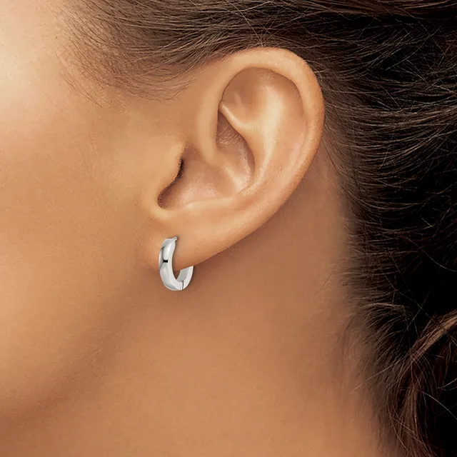 A person wearing a small polished silver curved hoop earring in their pierced earlobe, shown in profile view.